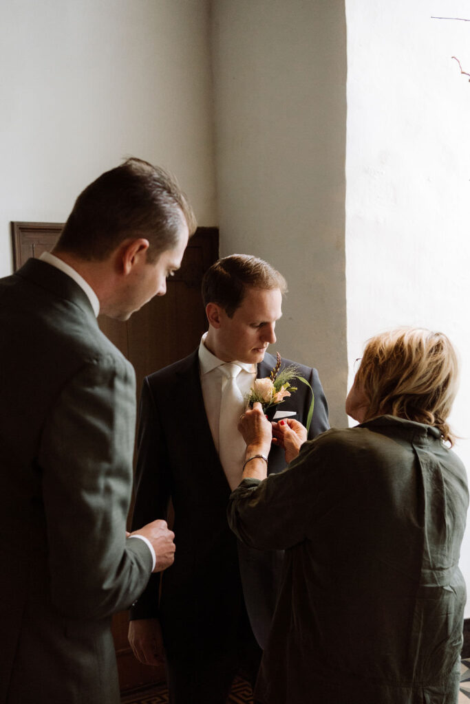 Getting ready bij slot doddendael. Moeder van de bruidegom helpt met de corsage. Beste vriend kijkt toe. 